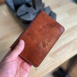 Reisepasshülle aus braun-rötlichem Leder, handgenäht für einen Reisepass, Scheckkarten oder Geldscheine, mit Logo Elch.